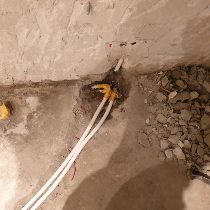 Reparerade värmerör som går i en ränna i betong med synliga kopplingar och kabeldragning.