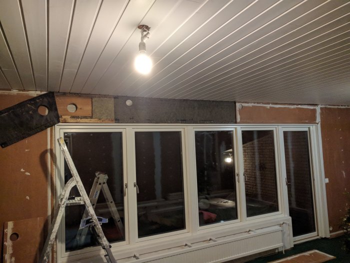 Inomhusbyggarbetsplats med öppet 110mm hål i bärlina ovanför fönster, stege och byggmaterial synligt.