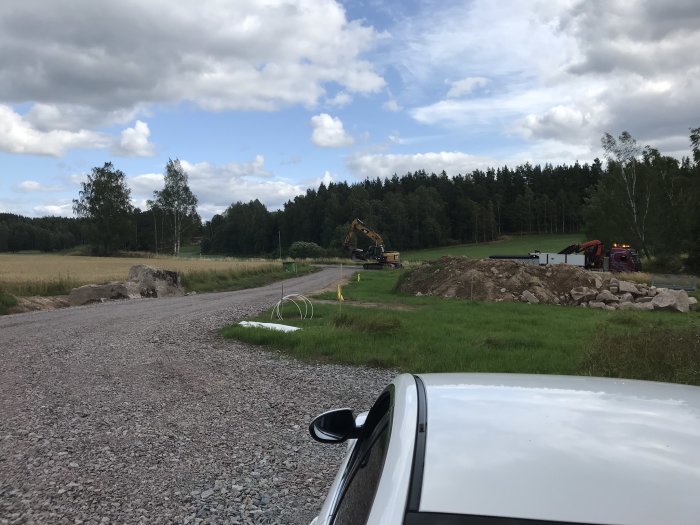 Grusväg med grävmaskiner vid schaktarbete för husgrund på en byggtomt, synlig bilhörn.