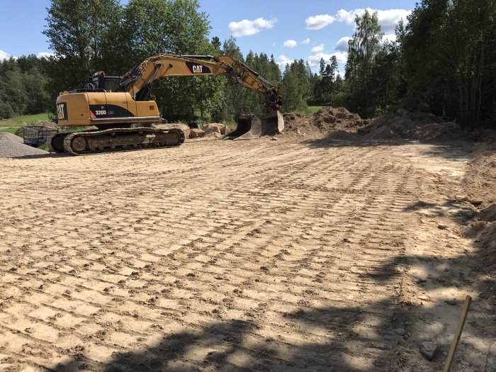 En grävmaskin på en plan byggarbetsplats där markarbeten för en husgrund just har genomförts.