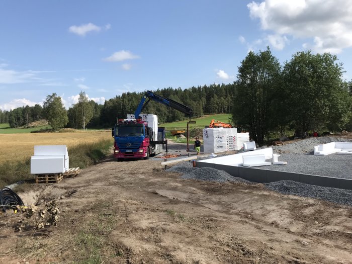 Schaktning för husgrund med en grävmaskin och lastbil vid ett byggprojekt på landsbygd.