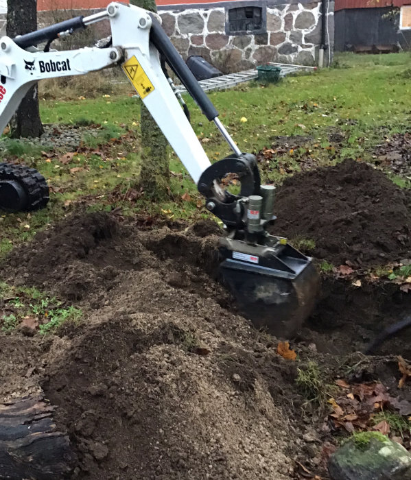 Minigrävare gräver i jord för att lägga om avloppet.