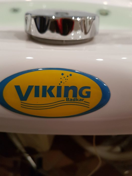 Logotyp för Viking Badkar på en vit badkarskant med en suddig kran i bakgrunden.