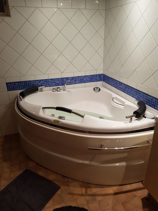 Hörnbadkar med jetsystem i ett kaklat badrum med blå dekorationsbård.