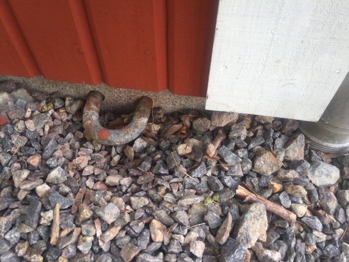 Inbäddad stöldögla i bottenplattan bredvid en byggnad, omgiven av småsten.