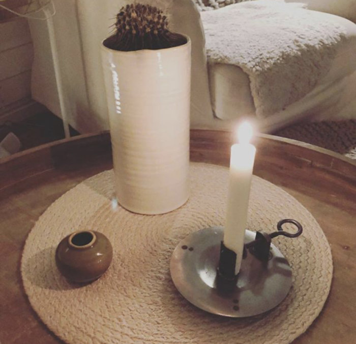 Ett brinnande handstöpt ljus i en metallisk ljusstake på ett bord med inredningsdetaljer.