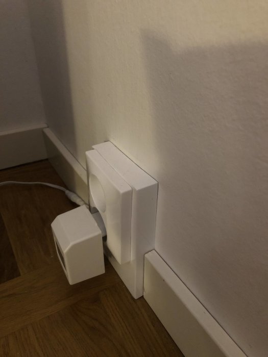 Vitmålad golvlist och vägg i hörn med 2K billack, bredvid eluttag och sladd.