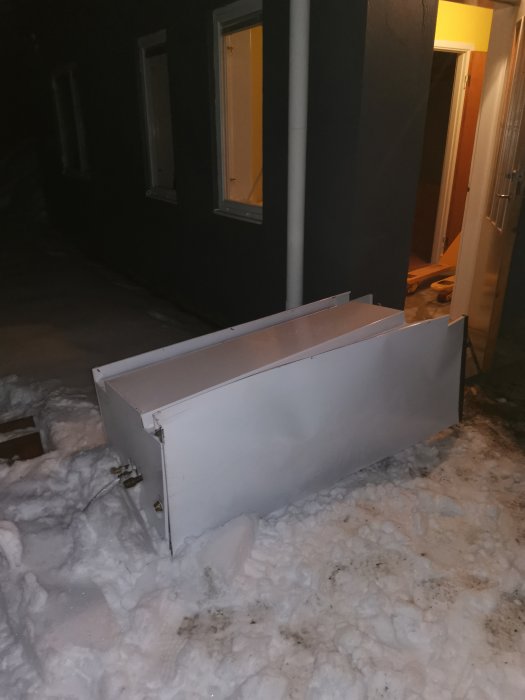 En stor acc-tank ligger i snön framför ett hus vid nattetid, efter att ha tagits ut ur huset.