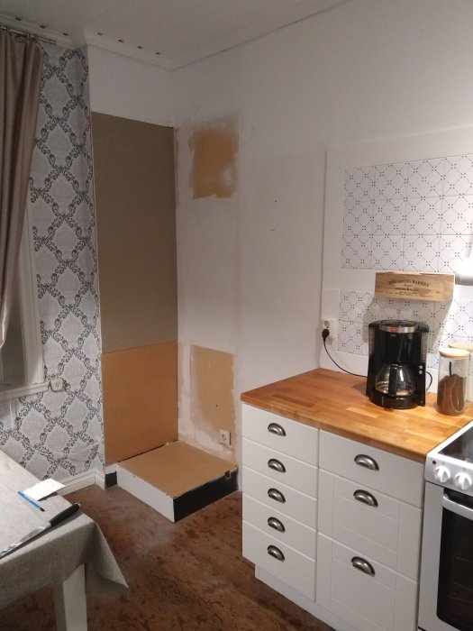 Kökshörn under renovering med borttaget högskåp, synligt reglarverk och omatchade bänkskivor på underskåp.