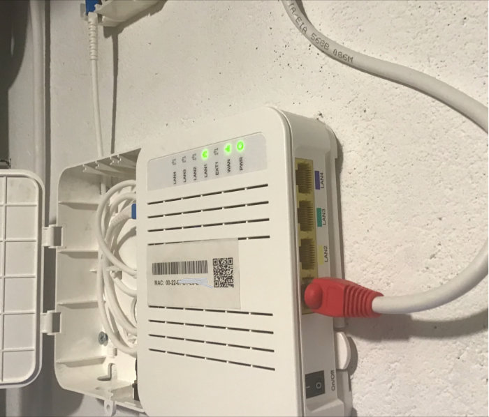 Öppen Telia fiberdosa med inkommande fiberduct ovanifrån och röd fiberpatchkabel.