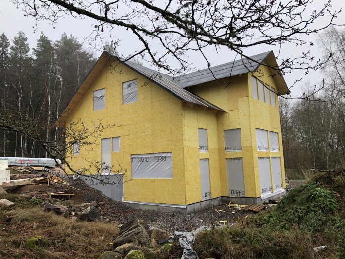 Ett hus under konstruktion med gul isolering och täckta fönsteröppningar.