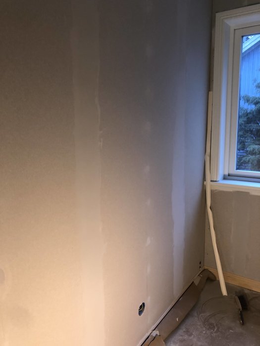 Ett rum under renovering med spacklade väggskarvar och skruvhål, redo för slipning innan målning.