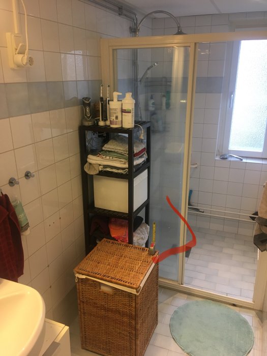 Badrum med duschhörna markerad med röd pil för att eventuellt placera tvättmaskin bredvid, mätband vid korg.