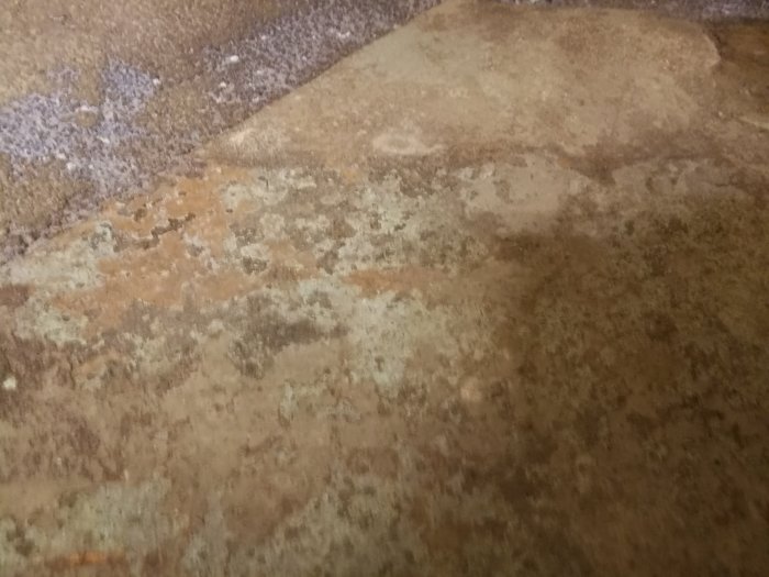 Gammalt klinkergolv med rester av gråbrun och grön färg, behov av reparation.