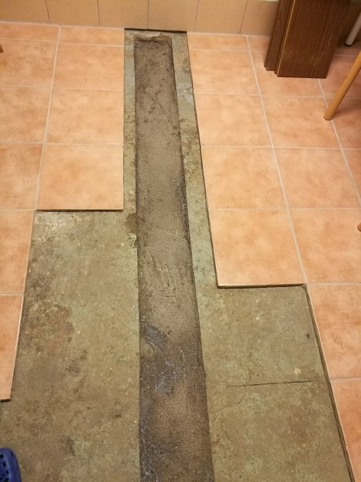 Klinkergolv med en upptagen sektion som avslöjar gammalt gråbrunt och grönt lager.