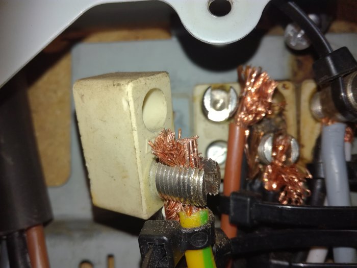 Trångt mätarskåp med skruvade plintar och flera ihoprullade koppartrådar.