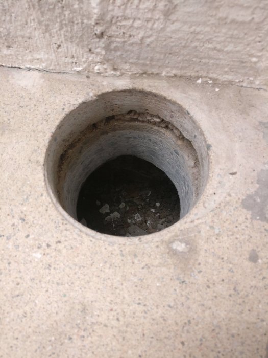 Borrad cirkulär öppning i en betongkällare visar ett underliggande tomrum och flerskiktat golv.