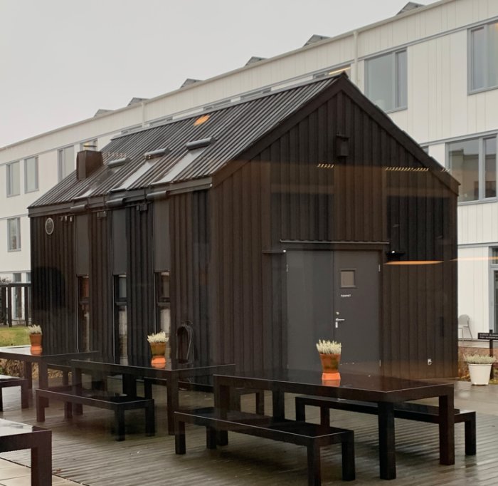 Modernt hus med mörk träfasad och tak utan överhäng under regnigt väder.
