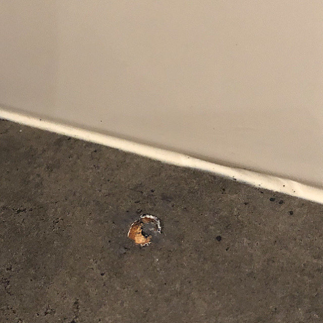 Ett par millimeter djupt hål i en grå betonggolv nära en vit vägg.