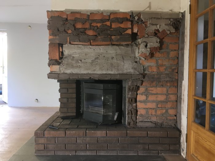 Delvis nedmonterad tegel eldstad med synliga hålrum och en installerad kassett.