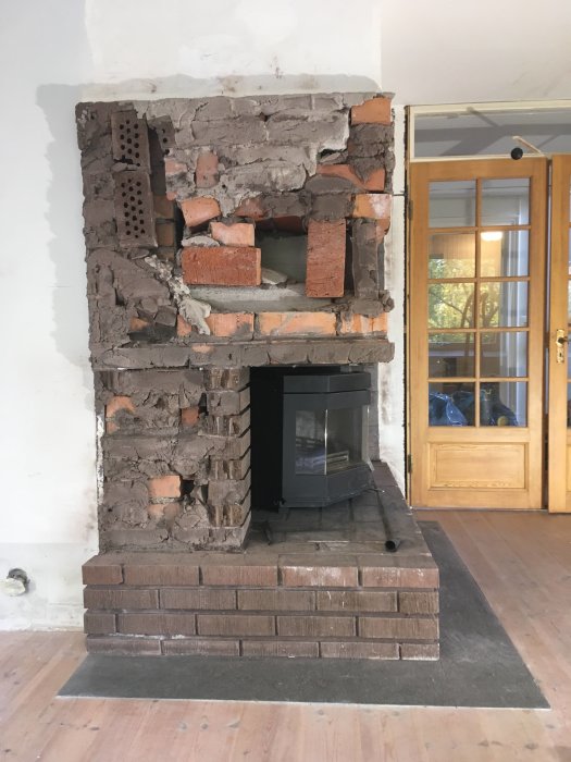 Eldstad med borttaget tegel som exponerar dess inre struktur och en svart kamin insats.