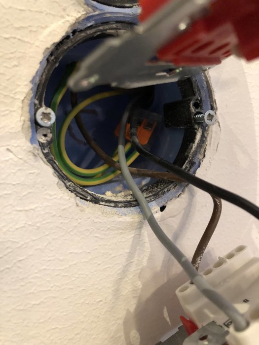 Eluttag med öppen kabeldragning som visar brun, blå och gul/grön tråd samt en delvis synlig lampknapp.