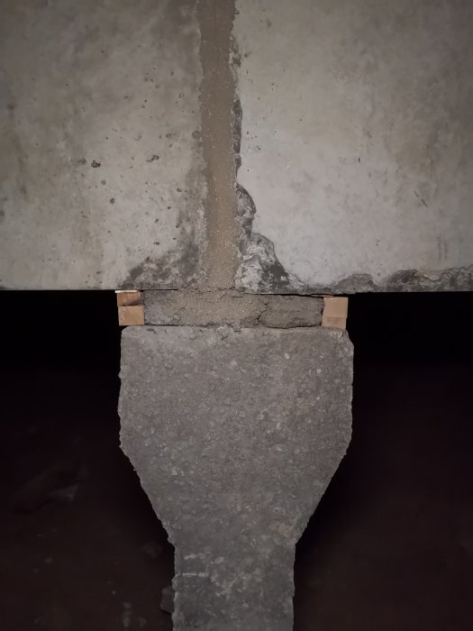 Betongplint med armeringsjärn och cement som förenar balk och plint, under krypgrund i hus.