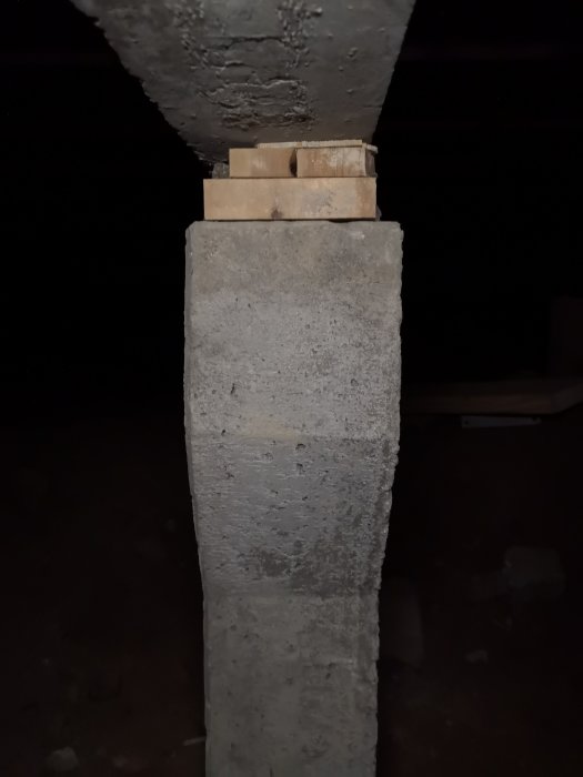 Betongplint med träklossar som stöder husets balkstruktur i en krypgrund.