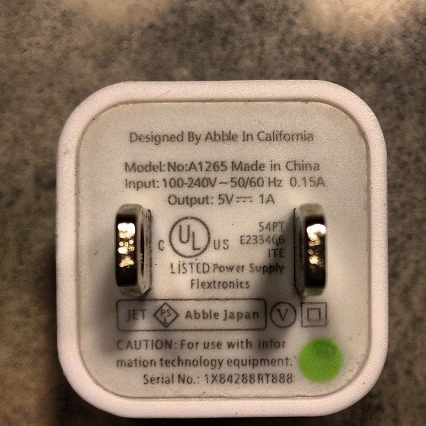 Vit laddare med texten "Designed by Abble in California" och specifikationer för en elektronisk enhet.