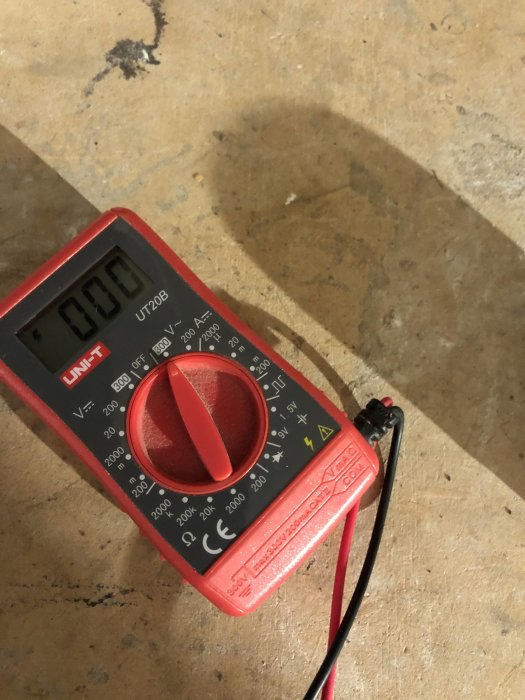 Digital multimeter på en betongyta, inställd på mätning med testledningar anslutna.