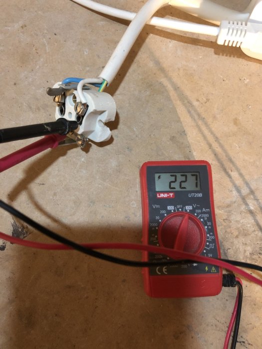 Multimeter som mäter spänning på en elkabel kopplad till en öppen kontakt, visar 227V.