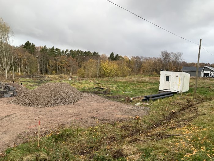 Tomt med nyligen fällda träd och en hög med grus, bredvid en förrådscontainer och rör på marken.