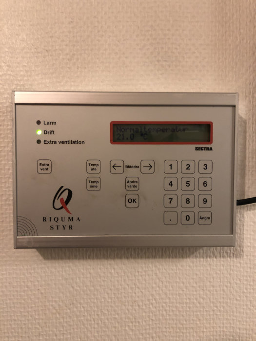 Kontrollpanel för RIQUMA FTX-aggregat visar normaltemperatur 21.0 °C på väggmonterad display.