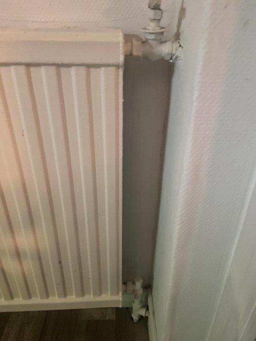 En gammal radiator kopplad med rör till tillflöde och retur i ett hus.