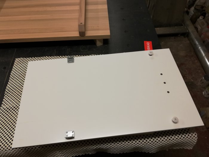 Vitlackad mdf-panel med infrästa neodymmagneter och epoxifyllda hål på en verkstadsbänk.