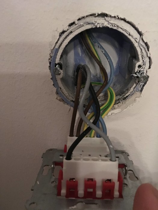 Elektrisk kopplingsdosa i vägg med brun, svart och flerfärgad kabel kopplad till en kontaktklämma.