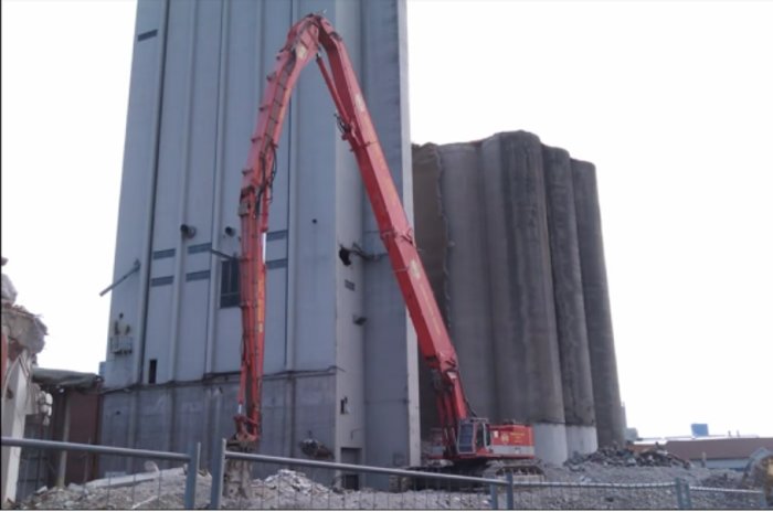 Röd betongpumpbil med utsträckt bom vid byggnadsrenovering.