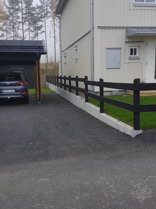 Staket monterat på L-stöd längs en uppfart bredvid ett hus och en carport.
