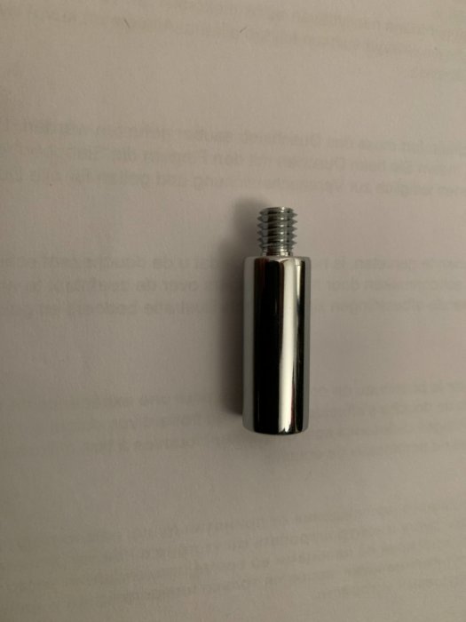 Oanvänd förlängningsdel till FMM takdusch med gängad mässingsända, ligger på ett vitt papper.