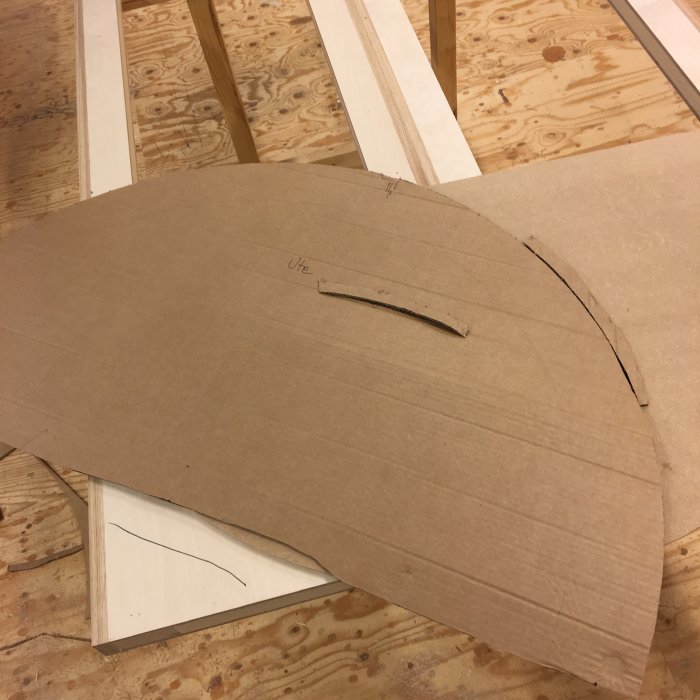 En mall i MDF för en gårdsdörr markerad med pennlinjer, vilandes på ett arbetsbord.