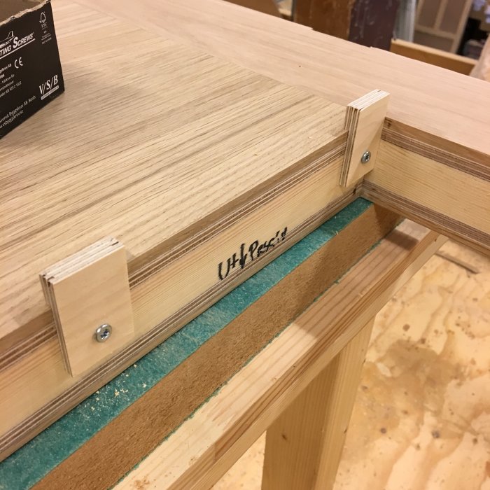 Falsad träpanel med infäst klots och skruv för glasningsarbete i dörrkonstruktion.