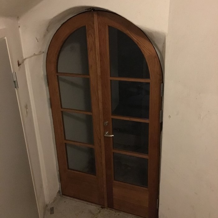 Böjd träkarmdörr med glasrutor monterad i vägg, redo för ytbehandling efter installation.