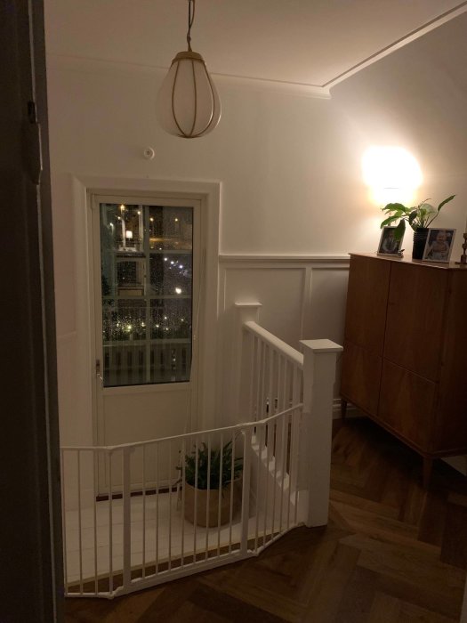 Renoverad hall på andra våningen med vit trappräcke, fiskbensparkett och en taklampa.