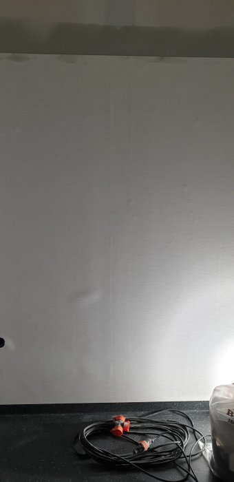 Oslipad vägg med synliga skarvar och ojämnheter efter mattläggares arbete, samt kabel på bänkskiva.