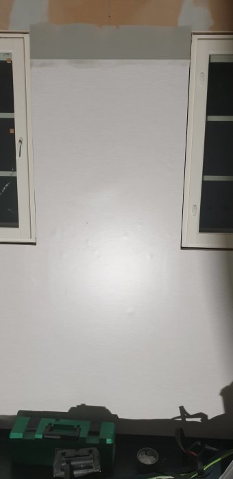 Vägg med synliga defekter, verktygslåda framför, dåligt tapetseringsarbete.