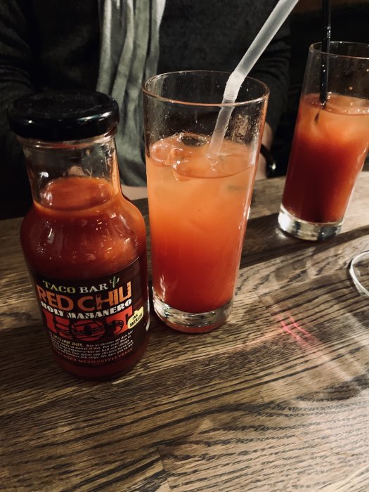 Två glas med Bloody Mary gjorda med röd chili sås istället för tomatjuice på ett bord.