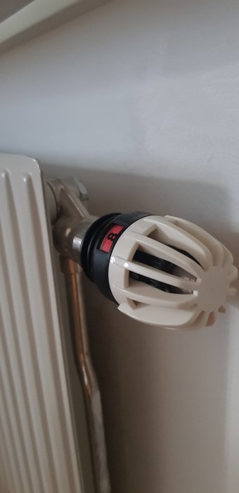 Termostat på radiator med inställningsmöjligheter, sannolikt toppen av en lång radiator.