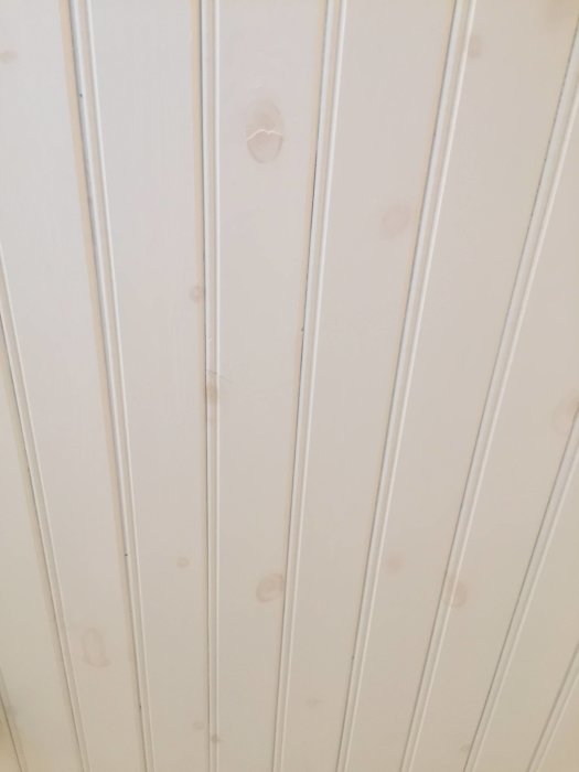 Vitmålad pärlspontvägg med synliga bruna kvistgenomslag.