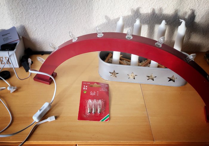 Röd halvcirkelformad lamphållare med ljuskällor ovanpå skrivbord, bredvid förpackning med extra glödlampor.