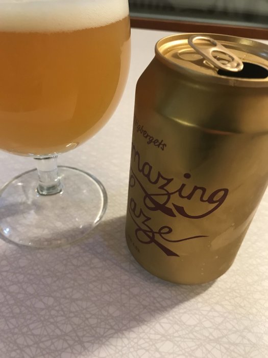 Öppnad burk av Amazing Haze öl bredvid ett glas fyllt med öl på ett mönstrat underlag.